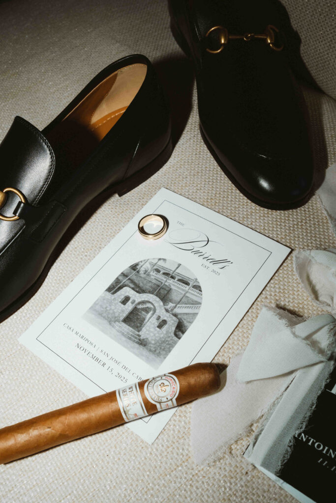 Groom's cigar, watch, and wedding invitation flat lay at Casa Mariposa Villa