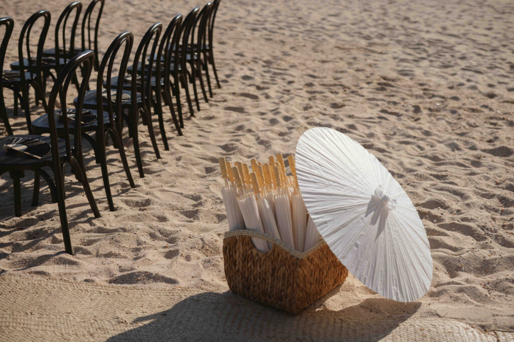Empty ceremony chairs on the beach with a woven parasol at Casa Mariposa Villa